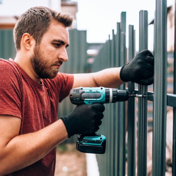 Handyman worker working at outdoor metal fence on new house construction site
